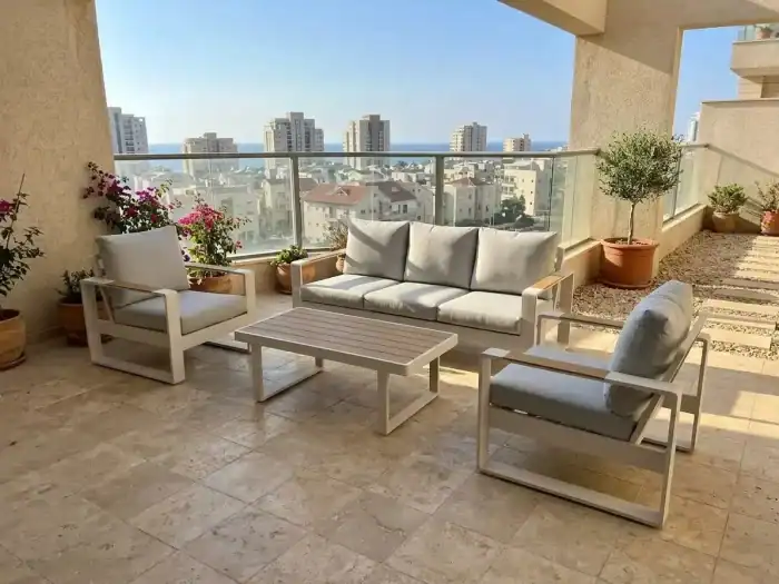 מרפסת חיצונית מודרנית עם ריהוט למרפסת בצהוב בהיר וכיסאות גינה, עציצים, ריצוף אריחים ומעקה זכוכית המשקיף על בנייני העיר ונוף רחוק של הים תחת שמיים בהירים.
