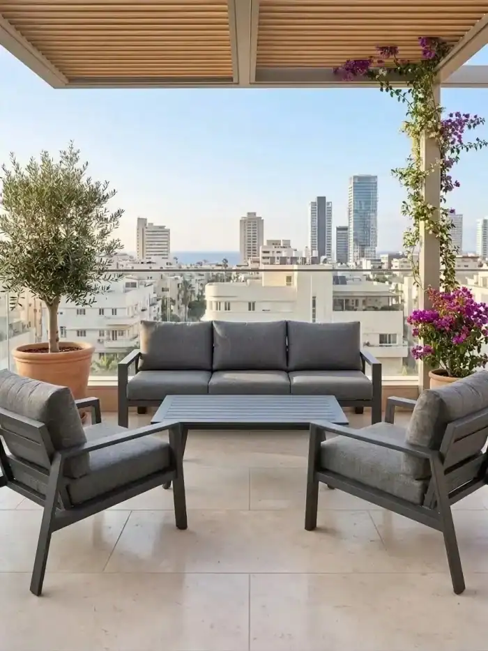 מרפסת חיצונית מודרנית עם מערכת ישיבה מאלומיניום מדגם LECCE, בעלת שלושה מושבים בצבע אפור, עציצים, ומגדלי העיר הנראים ברקע מתחת לפרגולה.