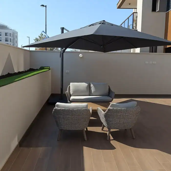 מרפסת חיצונית עם שני כיסאות, ספה קטנה ושמשייה טהיטית בגודל 4x3 על רצפת עץ, לצד קיר לבן ועציץ, הכוללת ריהוט למרפסת אלגנטי לנוחות מסוגננת בחוץ.