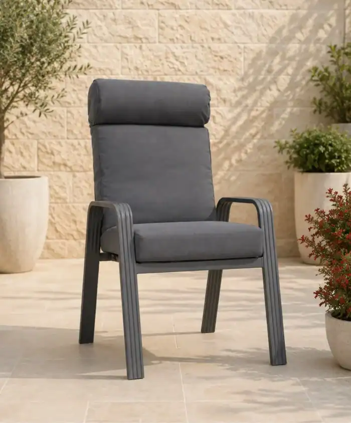 כיסא מדגם Trend בצבע אפור, עם ריפוד ומשענות יד, ממוקם על פטיו מרוצף, מוקף בעציצים ובקיר אבן בגוון בז', ויוצר אווירה מזמינה של ריהוט למרפסת.