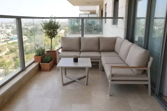פינת ישיבה פינתית מדגם “נייס” וכסאות גינה על מרפסת מרוצפת עם מעקה זכוכית; שולחנות גינה ועציצים ממוקמים בפינה ליד המעקה.
