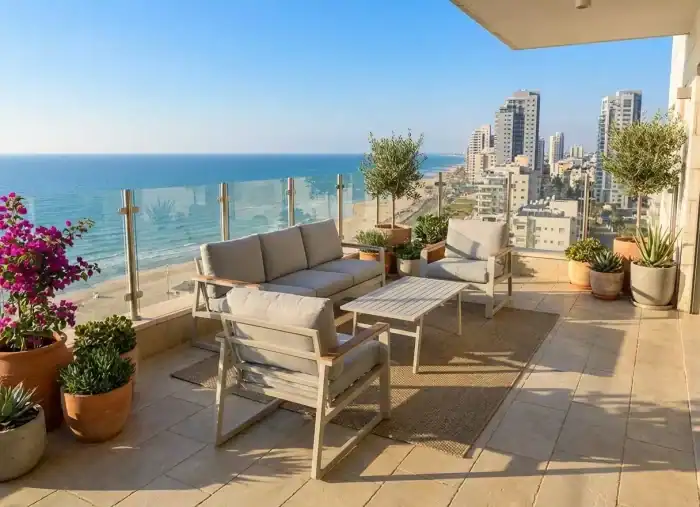 מרפסת מרוהטת הכוללת ריהוט גן, כיסאות גינה, פינות ישיבה, ונוף לים המשקיף על קו החוף העירוני עם בניינים רבי קומות תחת שמיים בהירים.